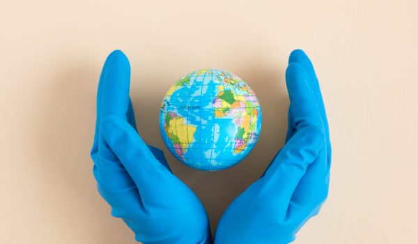 Earth globe in hands in blue protective glove on a clean beige background. The concept of protecting nature, ecology and global peace. World globe in Hand. The COVID-19 pandemic.