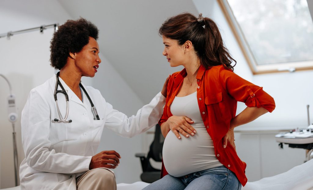 Doctor advising pregnant woman at hospital. A mid adult female doctor is in the office with a pregnant woman giving her advice about pregnancy.