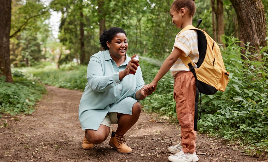 Side view portrait of black mother and daughter hiking together and using bug spray