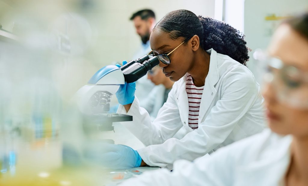 Black female scientist looking through microscope while working in laboratory.